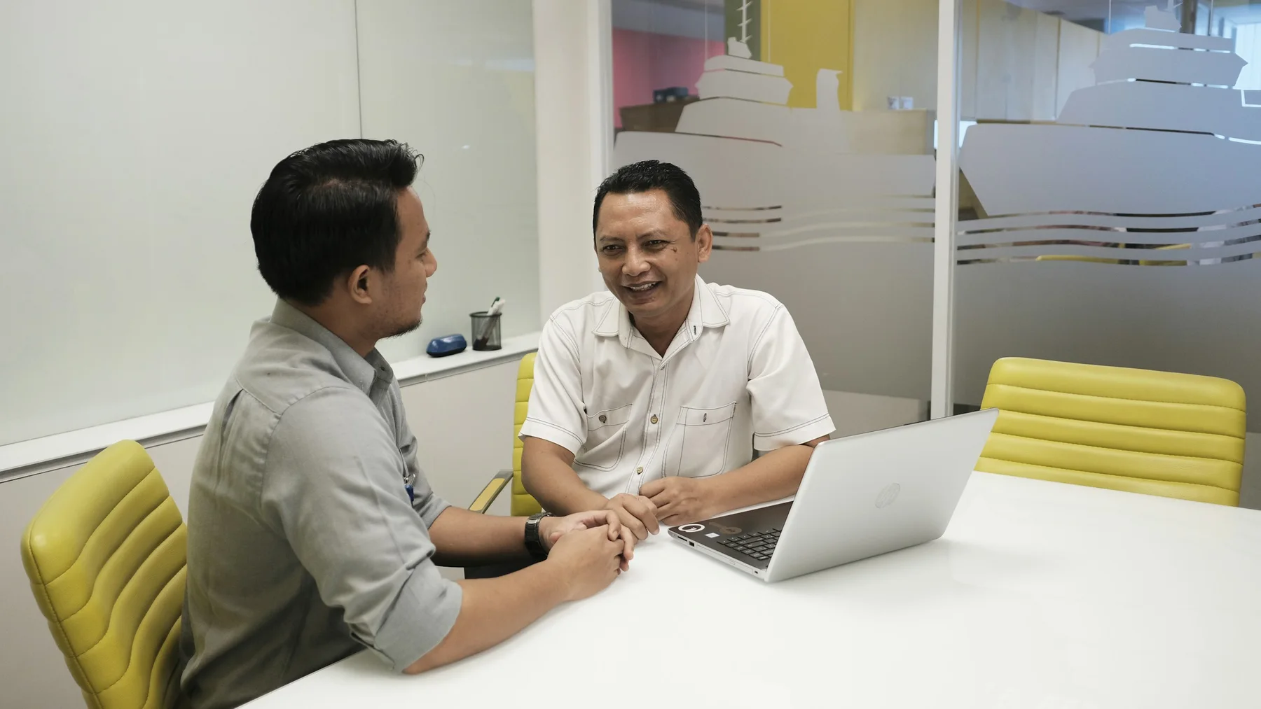 Dua pebisnis Indonesia berdiskusi di meja kantor dengan sebuah laptop
