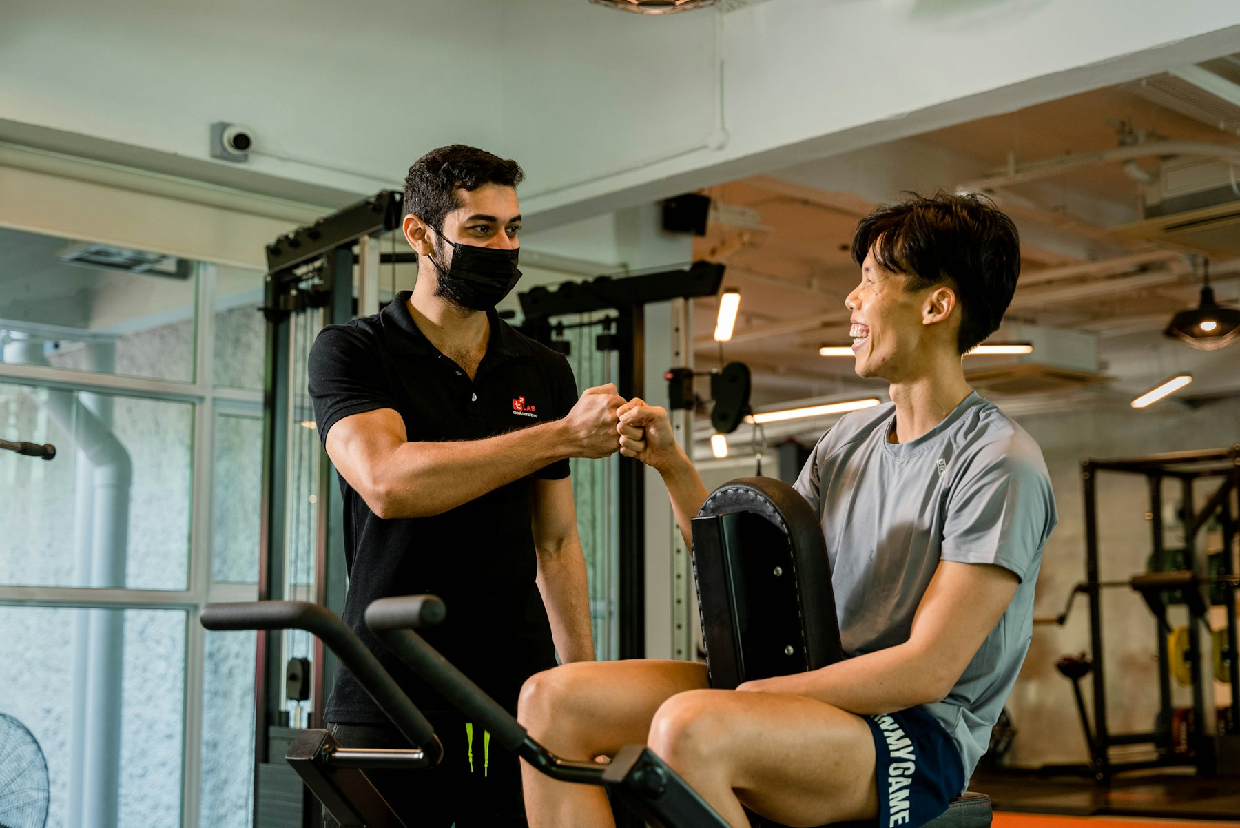 Personal trainer Asia sedang fist bump dengan klien di area gym setelah latihan