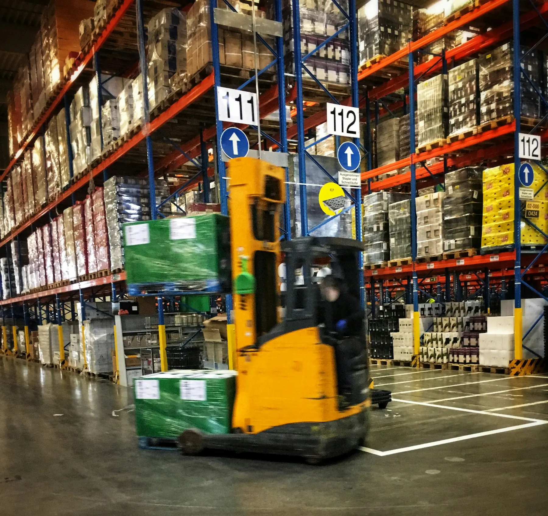Forklift bergerak di antara rak gudang