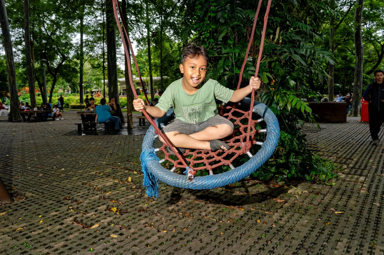Seorang anak bermain ayunan di taman Jakarta