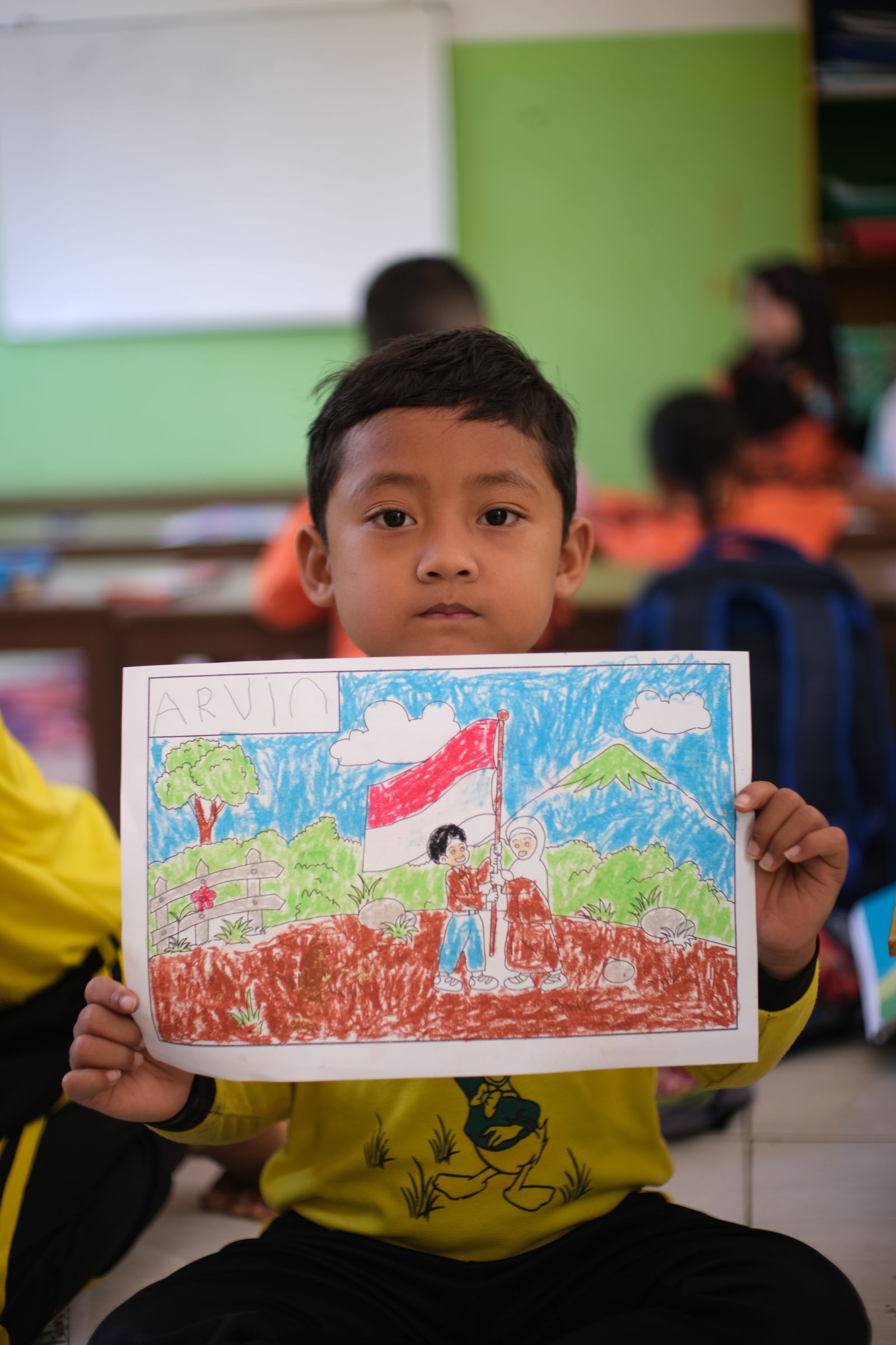 Seorang anak menunjukkan gambar yang dibuatnya